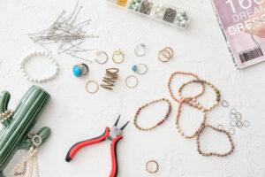 Workplace of jewelry designer with tools and beads on light background